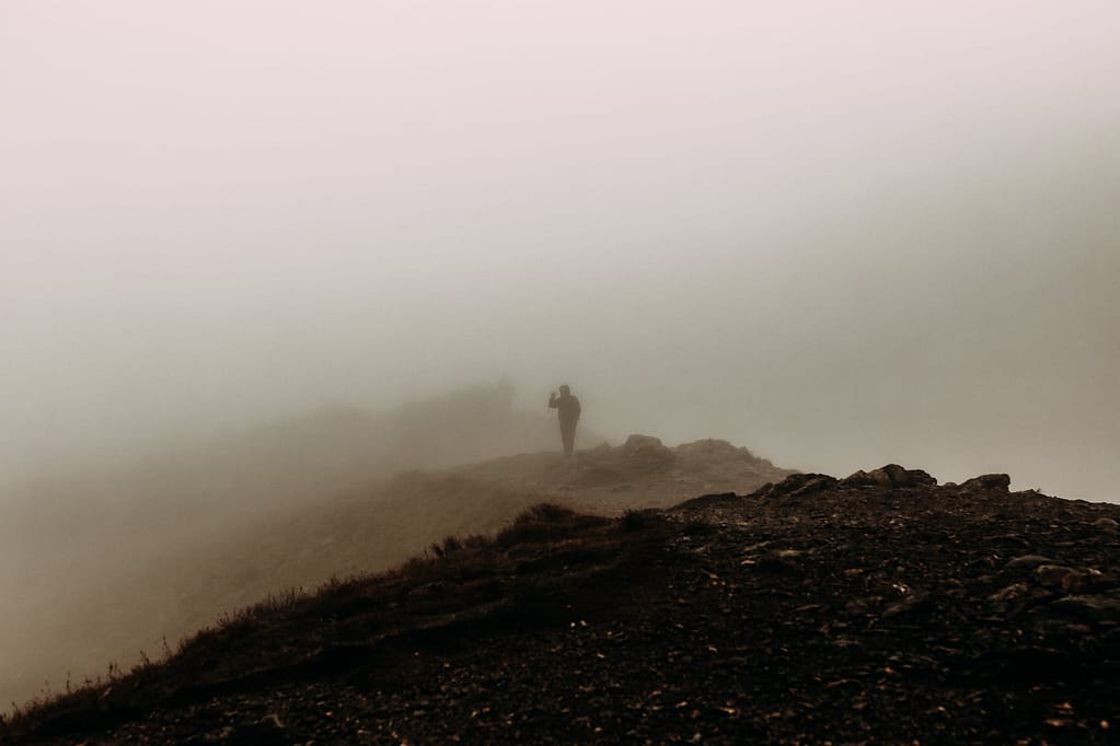 silhouette of person standing on hilltop in haze
